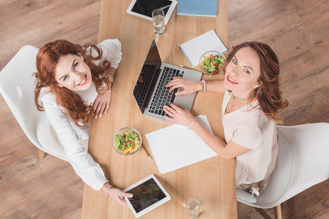 Photo of two young businesswomen working together and having lunch at the office