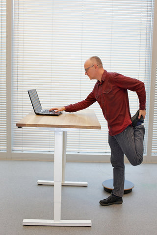 Photo of a middle-aged man in eyeglasses men with laptop at the mobile table doing the leg exercise 