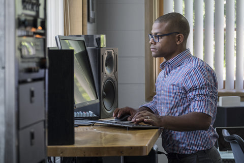 Photo of a young man standing at his computer desk 