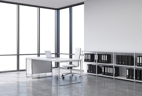 Photo of a workplace in a modern panoramic office. A white desk with a laptop, white leather chair and a bookshelf with black document folders.