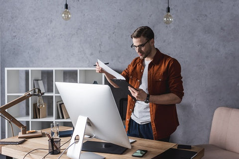 Photo of a serious young businessman, he is reading a document and  standing near a workplace