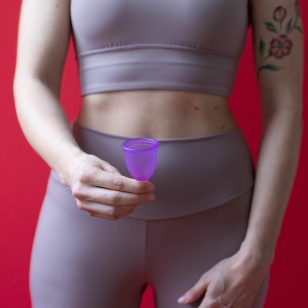 Person in workout clothes holding a purple menstrual cup