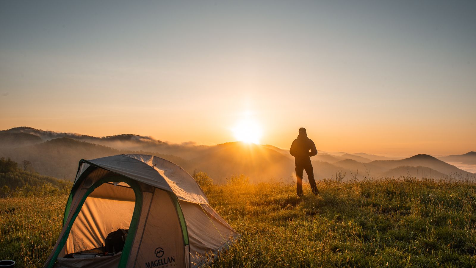 camper stands on a mountain looking at the sunrise