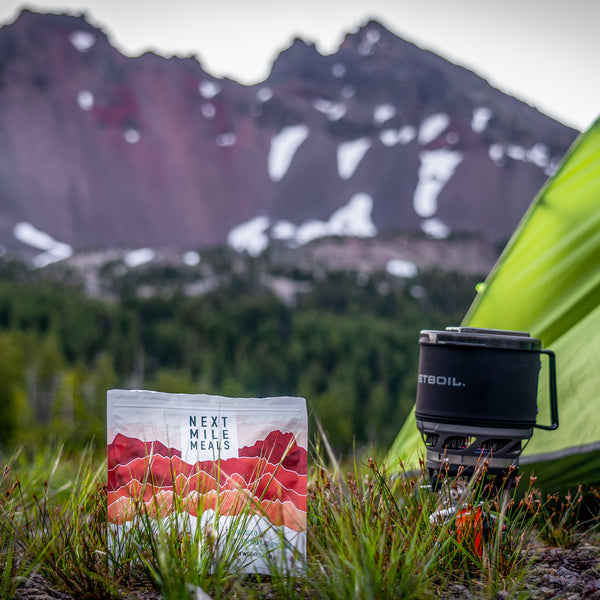 a backpacking meal in the grass next to a stove