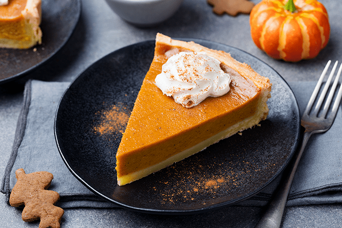 Slice of pumpkin pie with whipped cream and pumpkin spice garnish