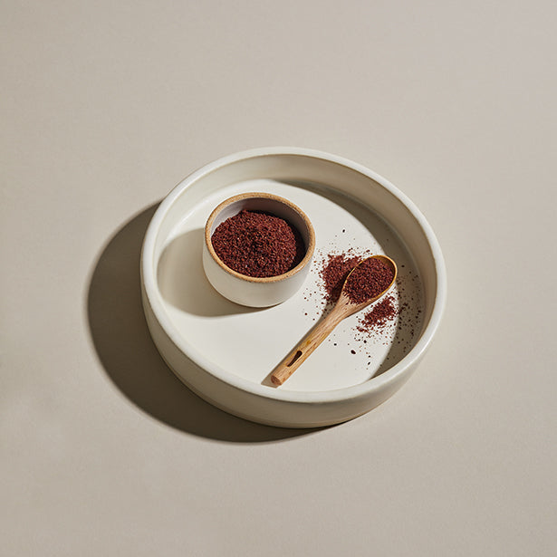 Sumac spice in a bowl with wooden spoon and plate.