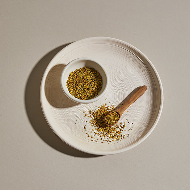 Fennel pollen spice in a bowl on a plate with a wooden spoon.