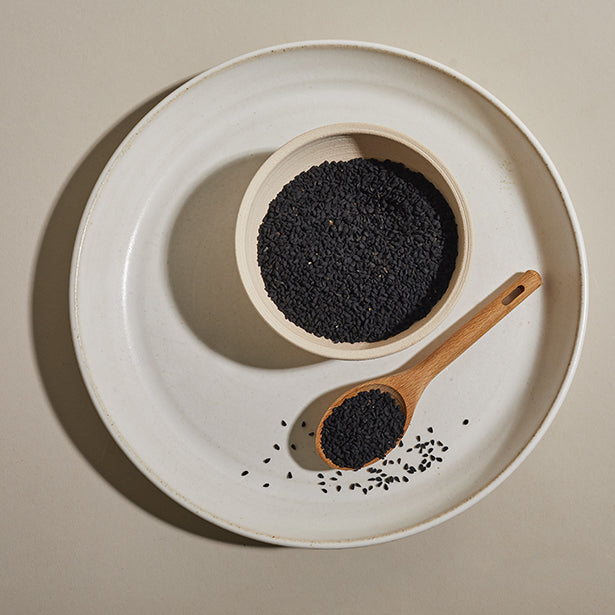 Charnuska seeds in a bowl on a plate with a wooden spoon.