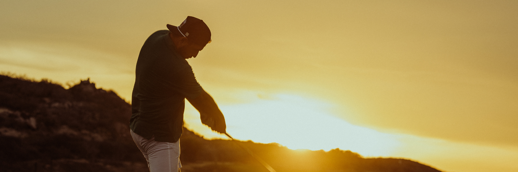 man hitting golf ball in the sunset