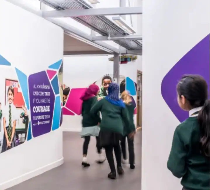 Students in green uniforms walking through a school hallway with colorful wall murals.