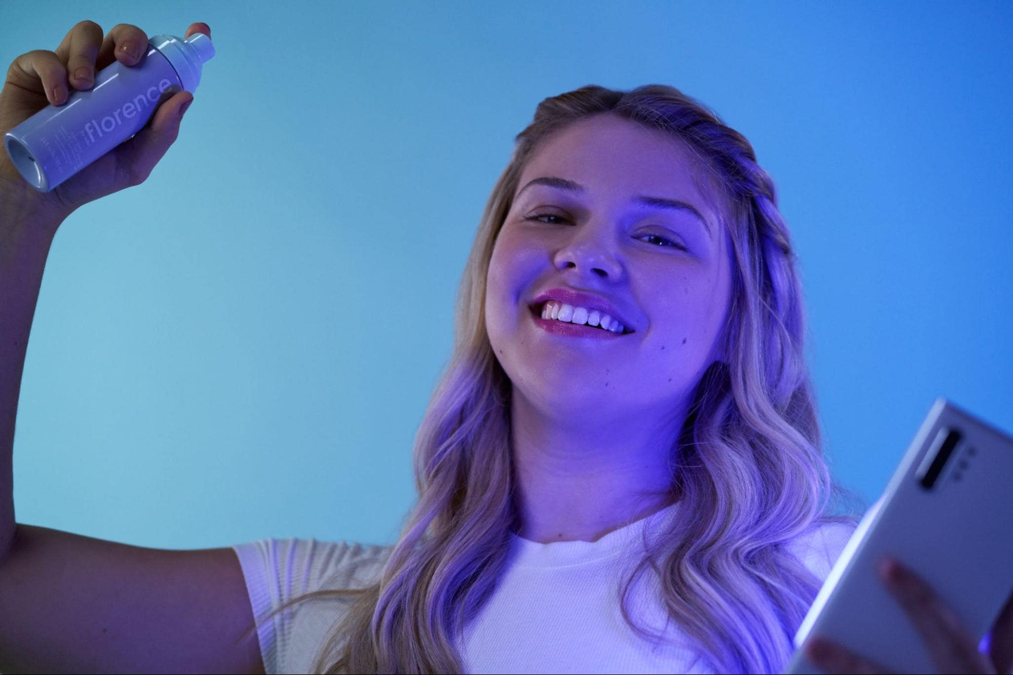 fbm model holding setting spray and phone under blue light
