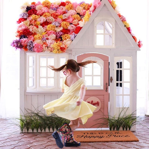 girl twirling in yellow dress in front of playhouse covered in pastel faux flowers