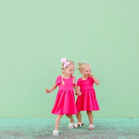 twins in matching pink twirl dresses standing in front of mint colored wall