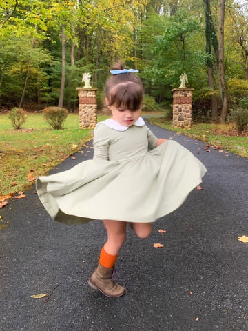toddler twirling in green dress, orange socks and boots with bow in hair