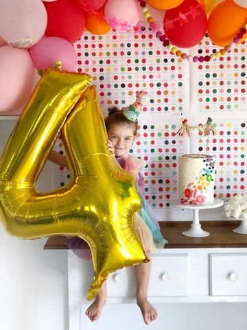 four year old holding number 4 balloon in rainbow dress for birthday party