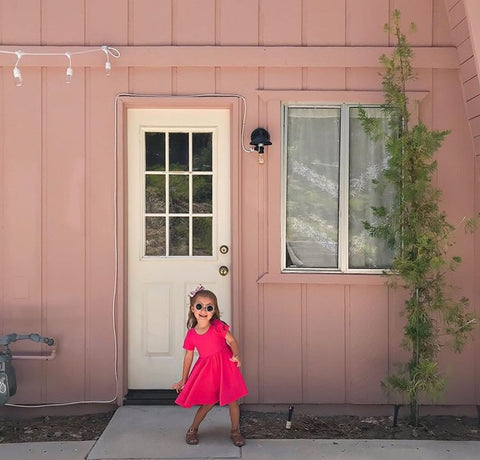 little girl in pink dress playing in front of a pink cabin