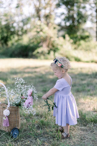 toddler in a field playing with a basket of flowers in a purple dress