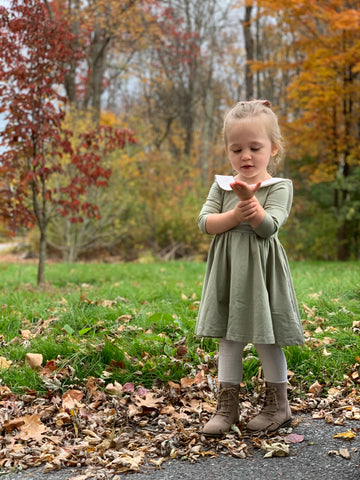 3 year old standing in field of leaves looking into her hand