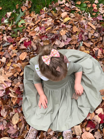 toddler sitting in a bed of fallen leaves in a cute twirl dress