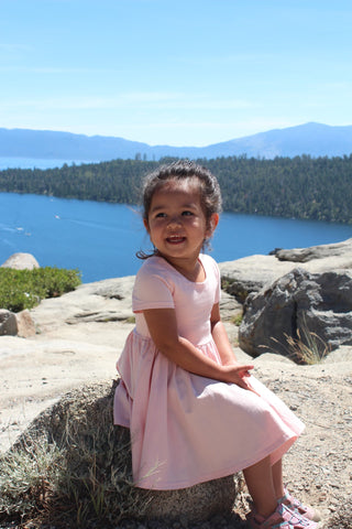 young girl in light pink dress sitting on rock in front of ocean