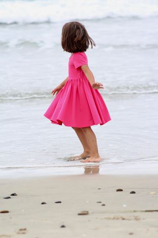 young girl in pink twirl dress playing on the beach shoreline