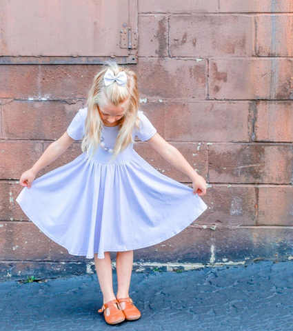 little girl in front of brick wall wearing lavender twirl dress