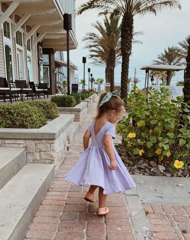 toddler girl walking down a sidewalk by the beach in a lavender twirling dress