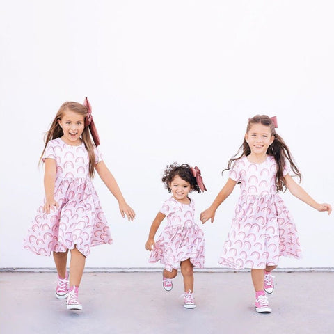 three girls running and playing in front of a white wall wearing rainbow dresses