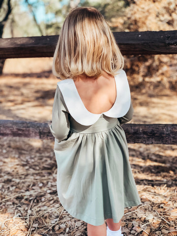 young girl standing near fence modeling back of her new dress