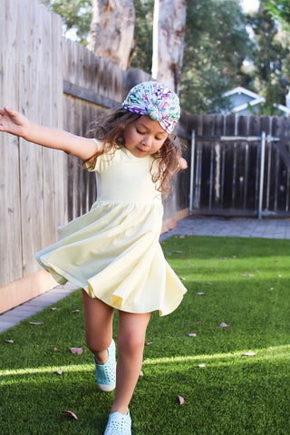 cute kid in yellow twirl dress and multi colored hair turban playing in backyard