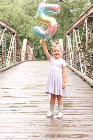 girl holding number 5 balloon and birthday hat standing on a bridge