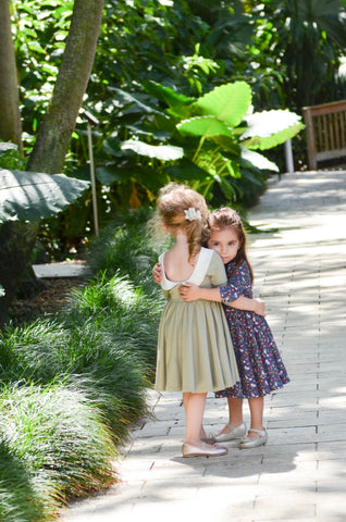 two toddlers hugging in a tropical setting wearing cute twirling dresses
