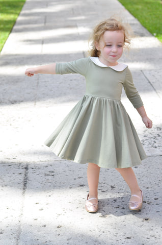 happy young blonde child spinning around on a path in a cute green dress