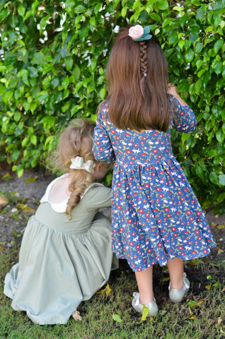 two 3 year old girls peeking through bushes in cute dresses