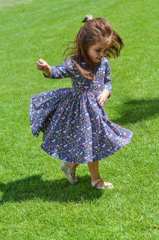 cute toddler girl playing on a field of grass in a vintage floral twirl dress and felt flower bow