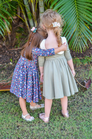 little girls hugging in front of greenery wearing cute twirly dresses