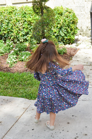 young brunette child twirling around in front of topiaries in a vintage floral dress