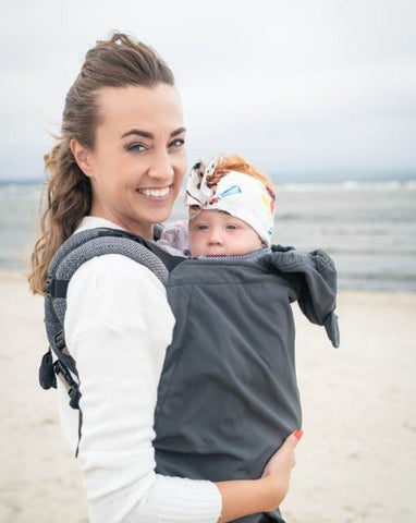 Model wears her baby with a babywearing cover available at Mama & Roo's
