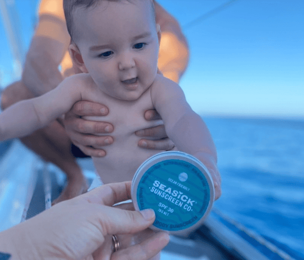 baby reaching for Seasick Sunscreen tin being handed to him while being held on a boat