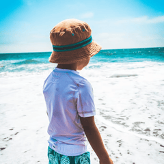 boy wearing hat and white rash top looking out to sea