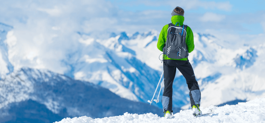 man wearing green ski jacket looking out over snow covered mountains