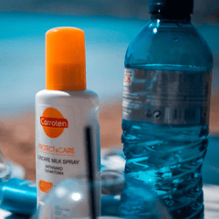 plastic sunscreen bottle with orange lid sitting next to plastic water bottle at the beach