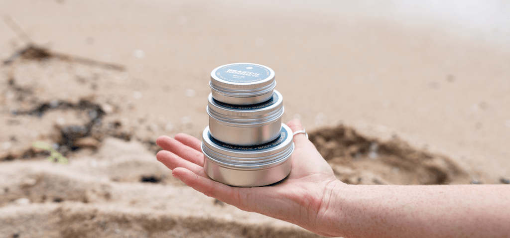 stack of three tins of sunscreen in an open palm with sandy background
