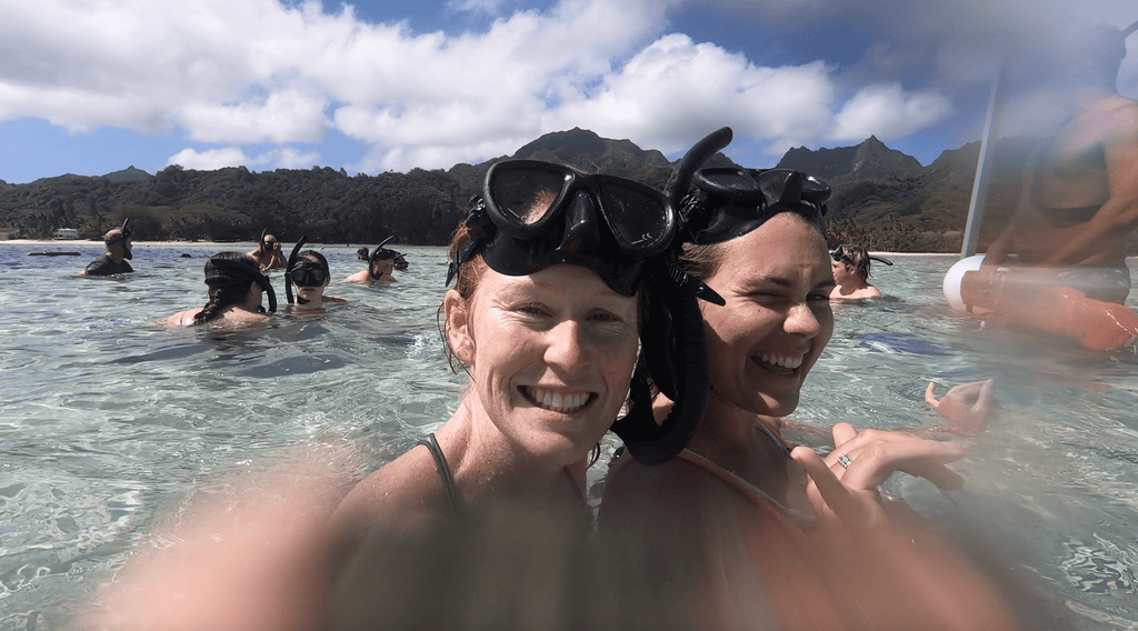 two women wearing snorkelling masks smiling while swimming in the ocean