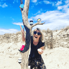 woman at the beach standing next to tall wooden driftwood with sunscreen
