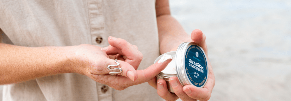 women's finger with sunscreen on it and a tin of sunscreen in her other hand