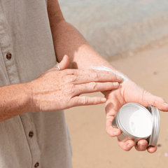 person rubbing sunscreen from a tin onto forearm at the beach