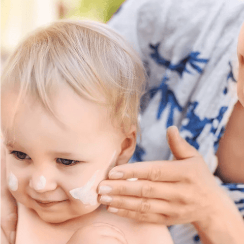 woman applies white sunscreen to the cheek of a blonde haired toddler