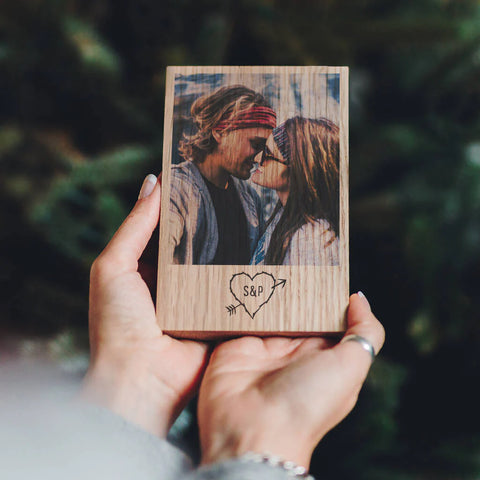 Two hands holding up an oak block with a photo of a happy couple printed onto the wood. A heart is featured underneath the photo, with the initials 'S & P' inside it.