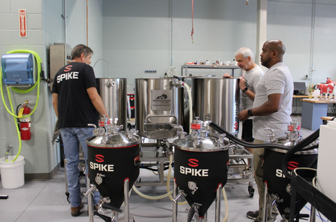 A group of men standing in front of a homebrew system at a brewery.
